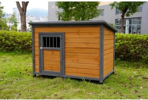Wooden dog house with a metal door on grass, with buildings and trees in the background