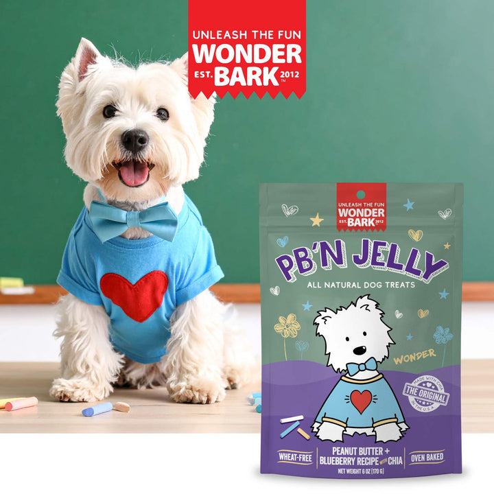 White dog wearing a blue shirt with a red heart next to a package of Wonder Bark PB&
